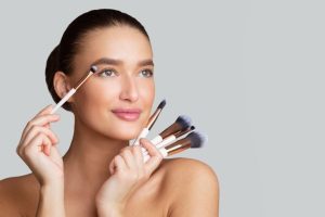 Mujer con maquillaje y artilugios de maquillaje en la mano