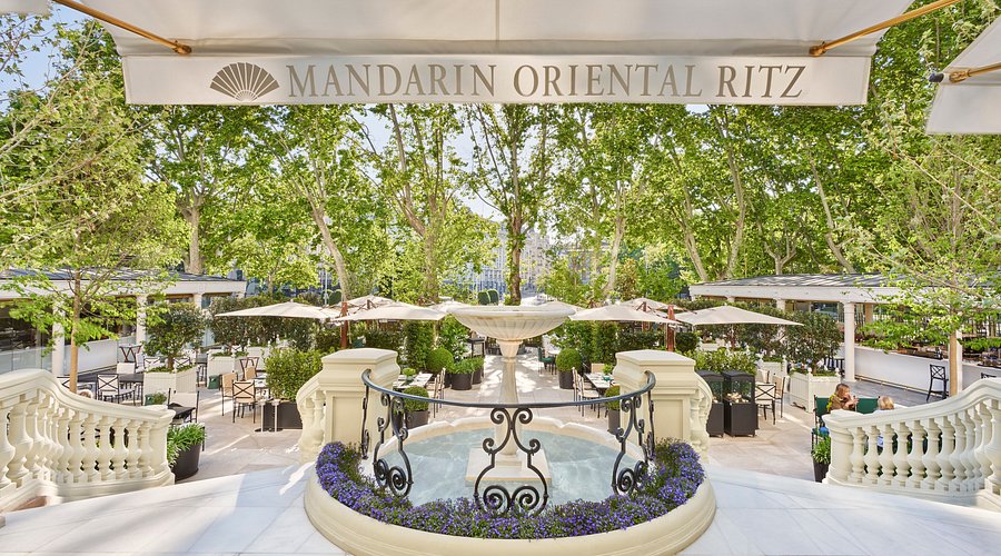 Vista de los elegantes jardines del Hotel Ritz en Madrid, con mesas al aire libre rodeadas de vegetación y ambiente sofisticado.