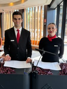 Azafatas/os bilingües facilitando la comunicación en un evento internacional, mostrando la importancia del personal bilingüe en entornos multiculturales.